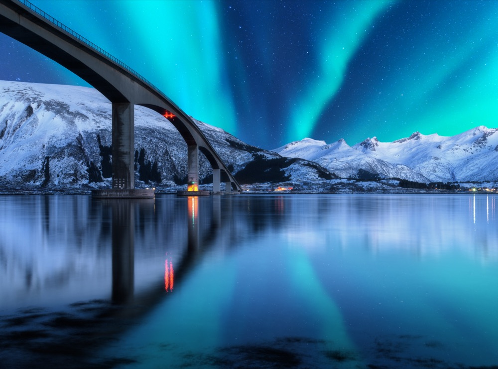 Polarlicht über einer Brücke und verschneiten Bergen in Norwegen